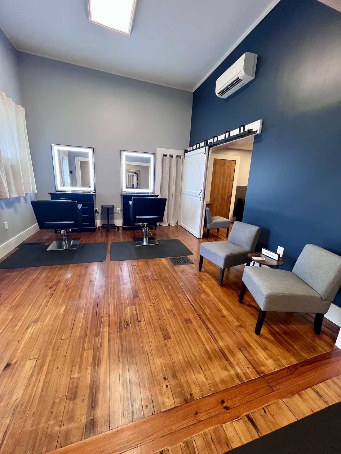 Styling area with vaulted ceiling, navy accent wall, and lighted mirrors at Mocksville House of Styles